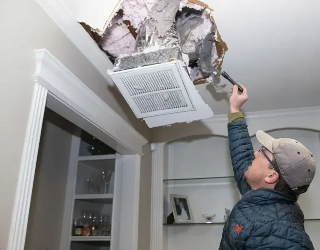 Inspector checking an opened ceiling around a vent for hidden water
