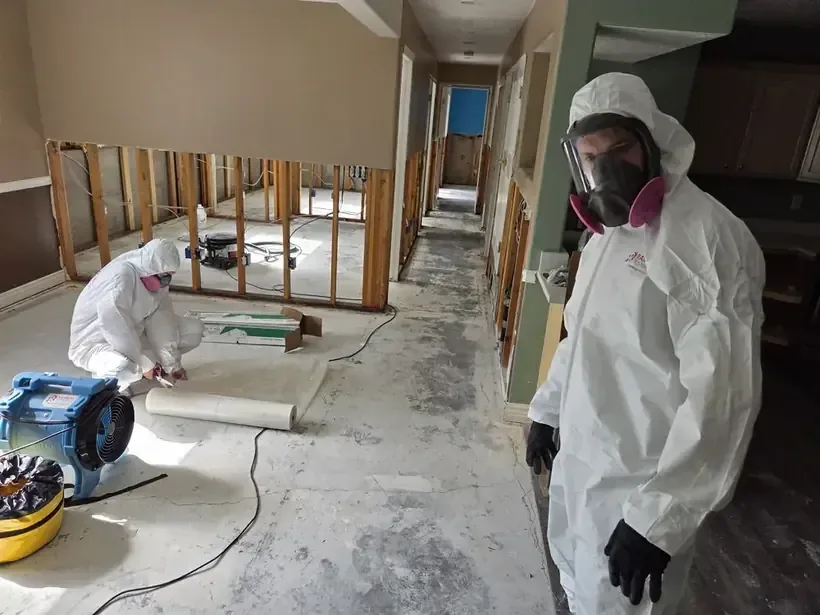 Crew in protective suits and masks cleaning up a sewage backup in a hallway opened to the studs