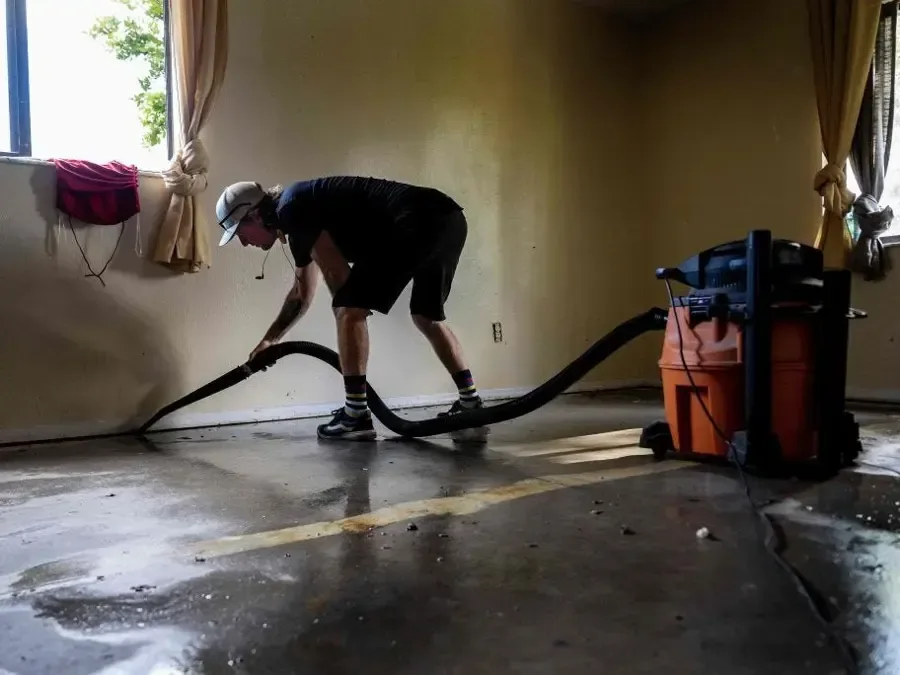 Wet vacuum hose pulling standing water off a bare concrete floor