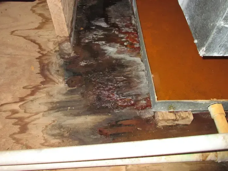 Rust and water staining across a floor beside a metal duct panel